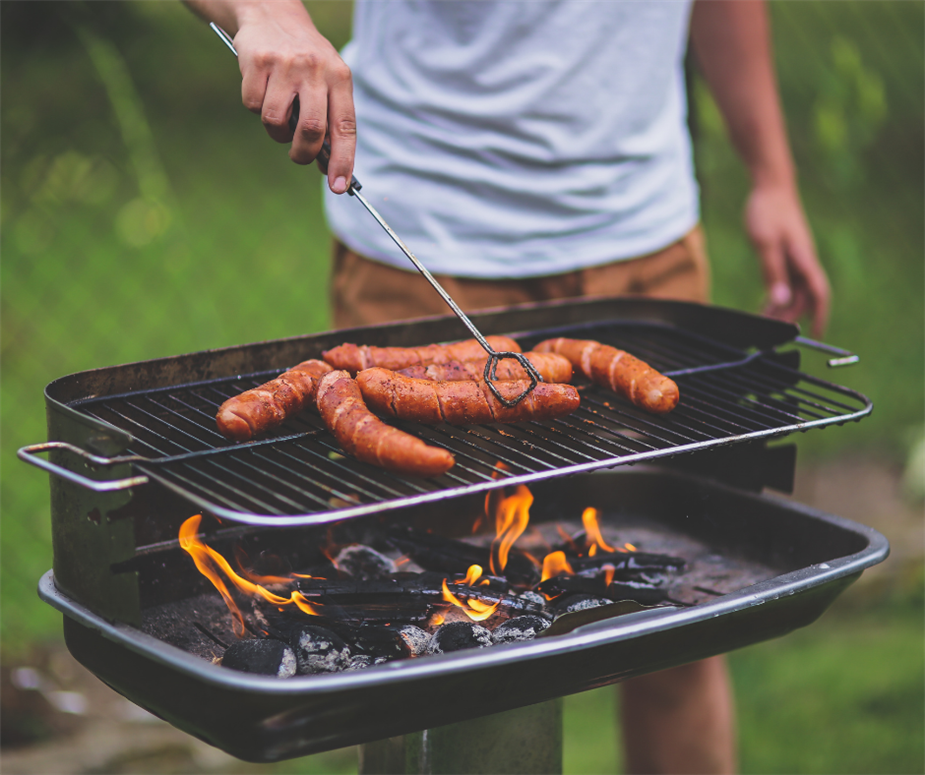 man turning sausages on an open charcoal grill